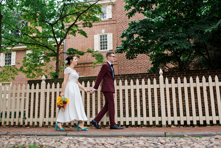 A groom walks his bride along a white fence in old city Philadelphia.